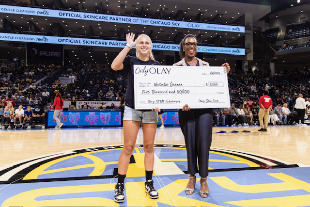 African American female Olay representative handing a large paper cheque board to Natalie Geenan to support her studies in biomedical engineering