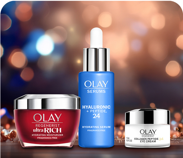 Olay Regenerist Ultra Rich Hydrating Moisturizer (red jar), Olay Serums Hyaluronic + Peptide 24 (blue pump), and Olay Regenerist Collagen Peptide 24 Eye Cream (white jar) arranged on a brown table with festive decorations and soft light in the background.
