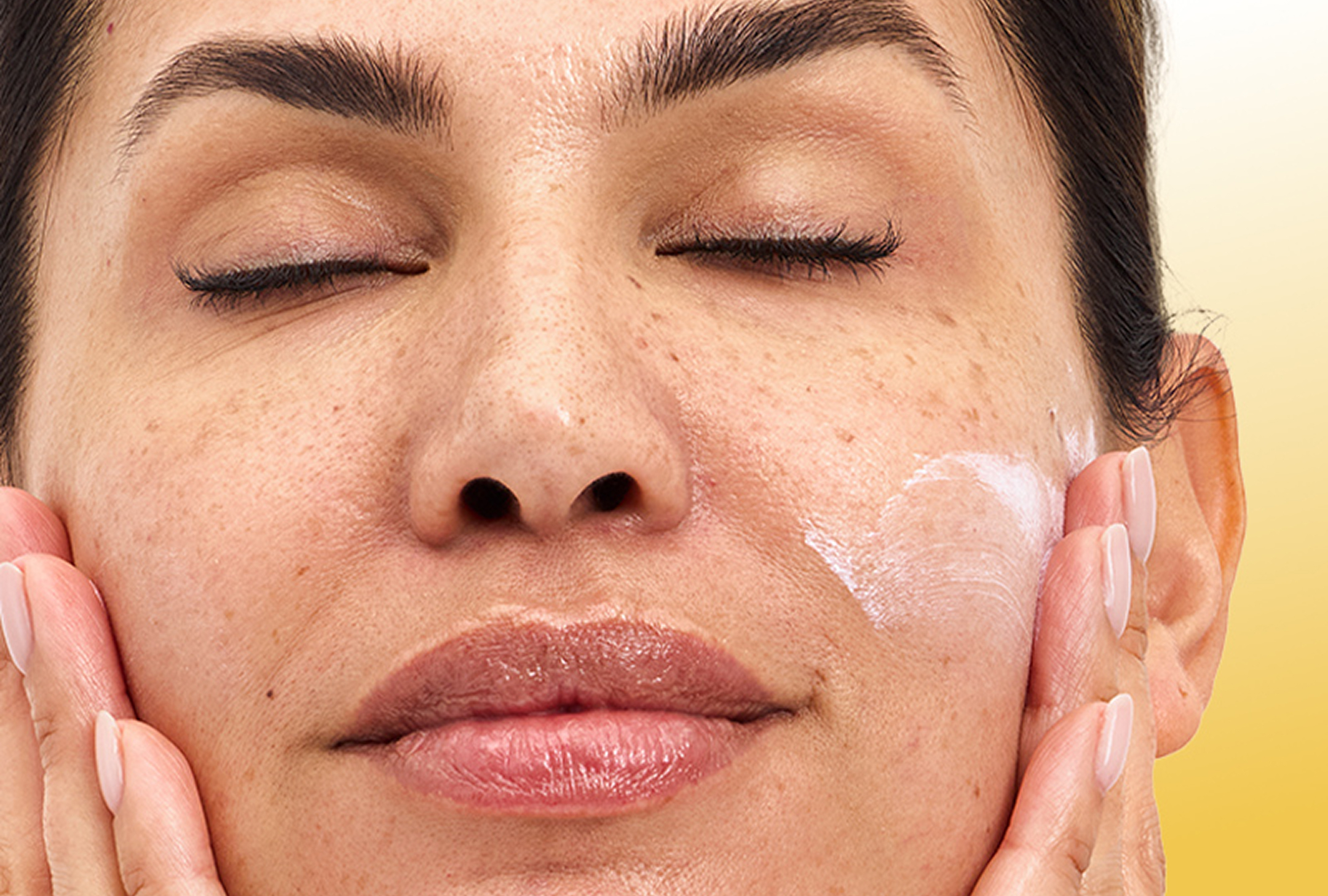 Woman clasping her face with both of her hands after applying Olay Complete+ Moisturizer with SPF 40 with a slight visible white cast to show it was just applied