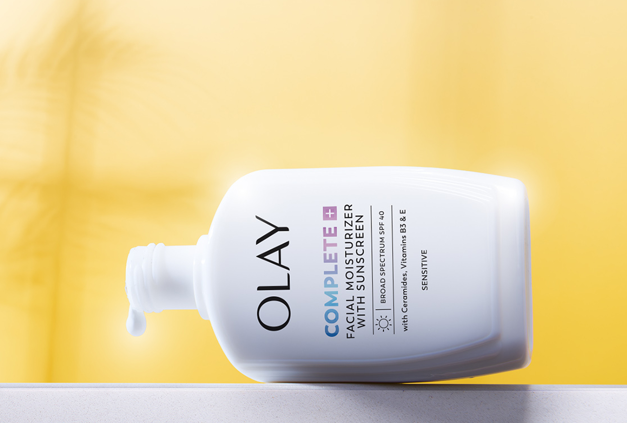  bottle of Olay Complete+ Moisturizer with SPF 40 resting on a white countertop on its side in front of a bright yellow fabric background
