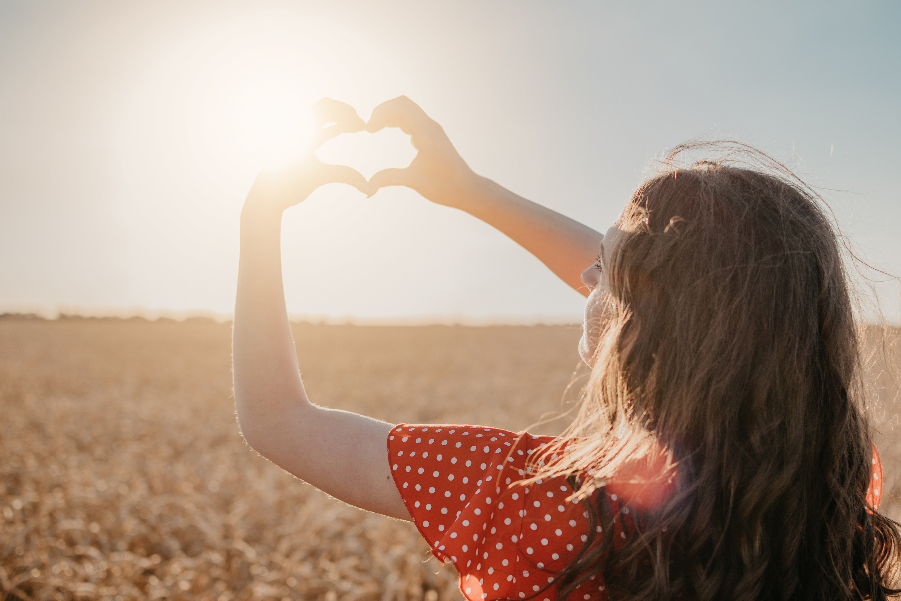 Woman holding hands up in shape of heart in front of sun