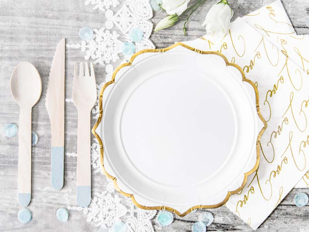 A decorative table setting featuring a gold-rimmed white paper plate, wooden utensils, pastel accents, and elegant napkins.