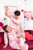 A couple in matching pajamas sits on a pink sofa surrounded by heart-shaped decorations, celebrating with confetti and drinks.