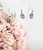 Earring – Light grey hanging pearl with clear bow, silver outline