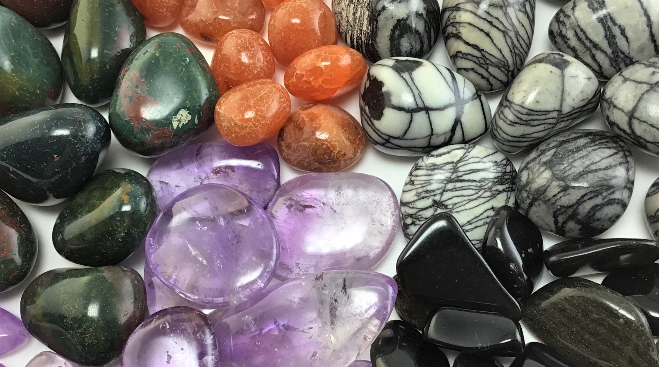 Tumbled crystals for Halloween in a radial pattern, including Amethyst, Bloodstone, Carnelian, Sheen Obsidian, and Spiderweb Jasper.