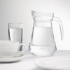 Olympia Glass Jugs 1Ltr with content, glass of water, cups and saucer, and plates on table.