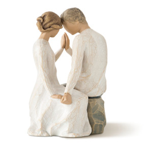 Male and female couple sitting across from each other touching heads and hands, male in dark pants, female in cream dress