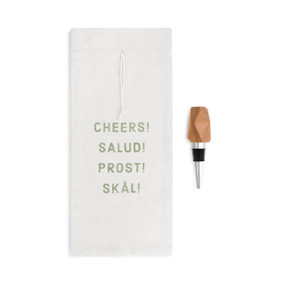 A white wine bottle bag that reads "cheers! salud! prost! skal!" in green letters beside a wooden wine stopper.