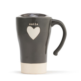 A tapered, charcoal, ceramic travel coffee mug, with a thick cream stripe base, a single cream heart in the center, and reads smile" in a cream typewriter font. With a handle, and lid placed on top."