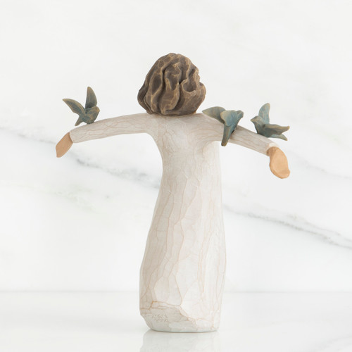 Back view of brunette girl figurine in white dress holding up arms with light blue birds on them