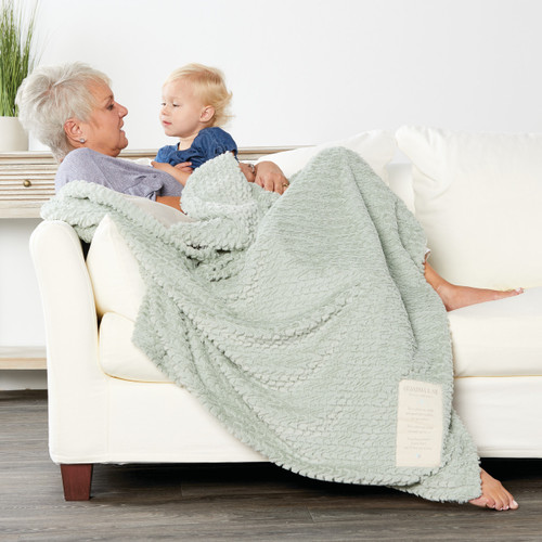 Far side view of older woman wrapped in blue blanket holding young blonde boy on white couch