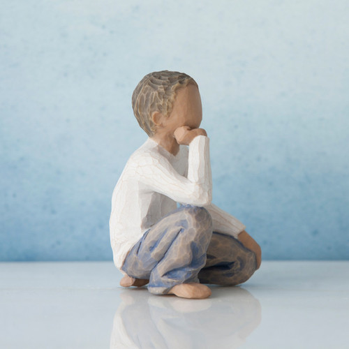 Small brunette boy figurine sitting with elbow on knee - wearing white shirt and blue jeans - blue background