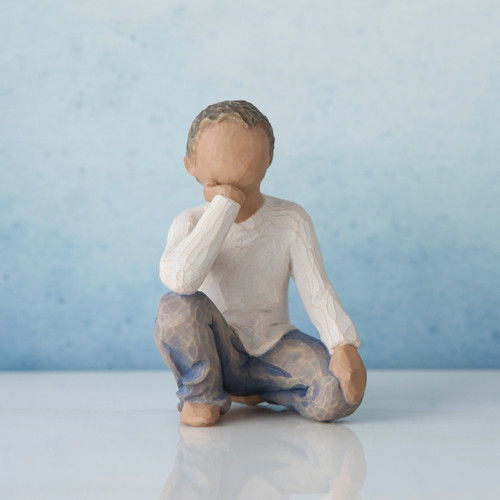 Small faceless boy figurine kneeling facing forward with one elbow on knee - in white shirt and blue jeans