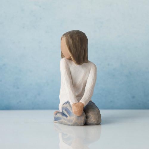 Small brunette girl figurine in white shirt and blue jeans with hands her on knees facing to the side - blue background