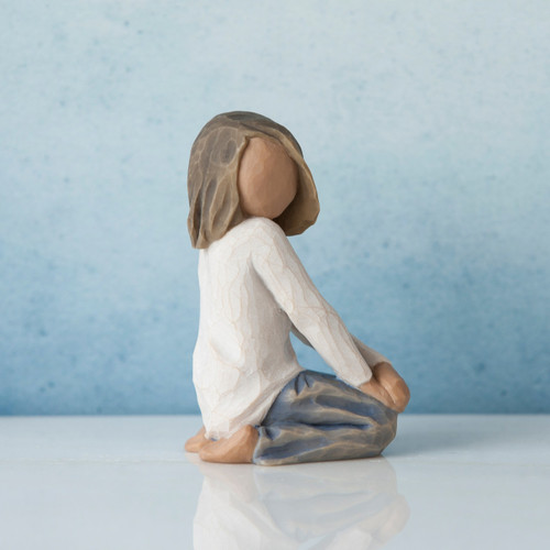 Small brunette girl figurine in white shirt and blue jeans facing the side on her knees - blue background