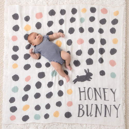 Large white blanket with grey, yellow, pink, blue polka dots - small baby laying down in the middle of it - and 'honey bunny' written on the right lower corner