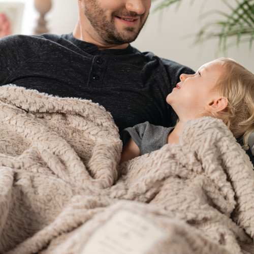 young girl smiling at father underneath tan plush blanket