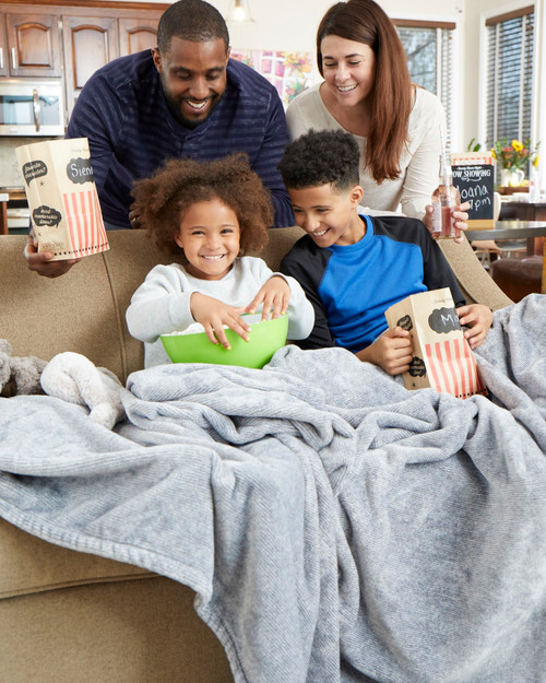 Mom and father leaning over smiling on two kids sitting on couch laughing eating popcorn