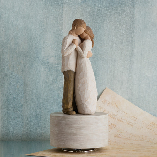 Faceless woman and man figurine wearing white hugging one another - standing on round white wooden plaque - blue background on music sheet