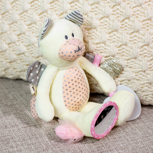 A light yellow plush cat with different sensory elements on its arms and paws. It also has a gray teether attached and is displayed sitting on a couch by a blanket.