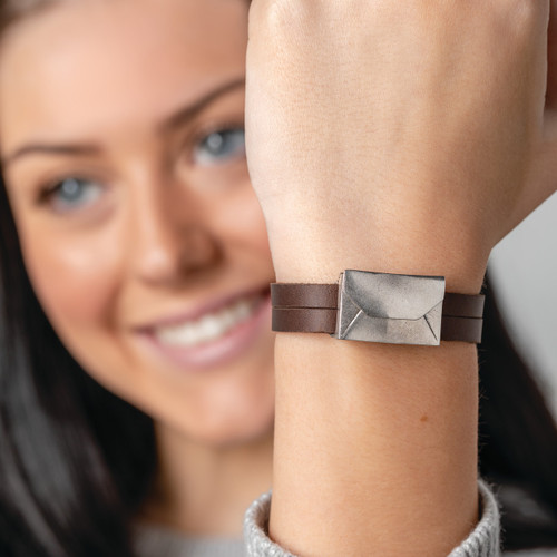 woman holding up wrist with leather wrap bracelet with silver envelope charm with her face in background out of focus