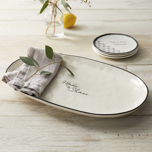 white ceramic oval shaped dish reading Made to Share with stack of plates in background