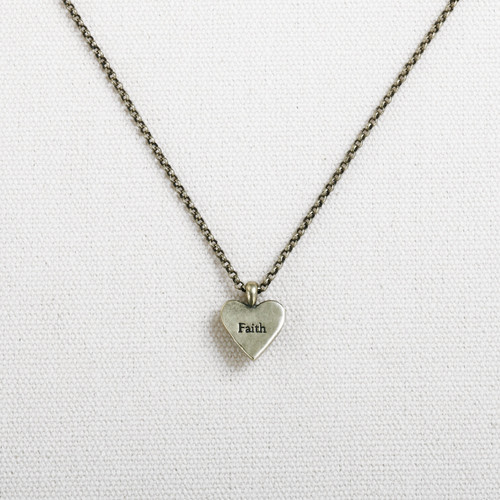 Close view of gold necklace with small heart pendant that says 'faith' on it