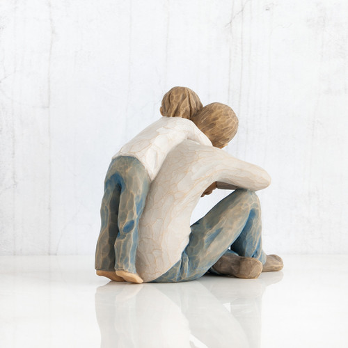 Little boy and man figurine facing away from the camera hugging one another wearing light blue jeans and white shirts