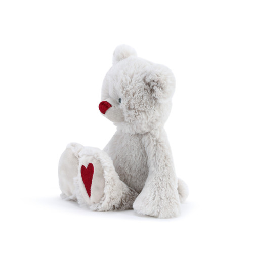 A side view of a fluffy white plush bear with a dark red nose and a dark red heart on the foot.