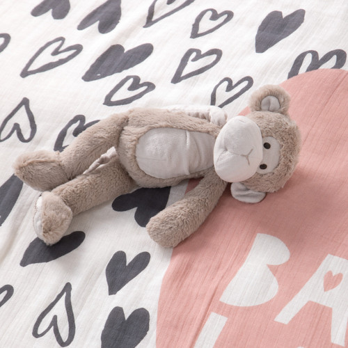 Light brown stuffed monkey animal laying on white / grey heart printed blanket