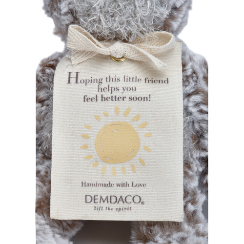 Close view of cream tag that says 'hoping this little friend helps you feel better soon' on grey stufed animal