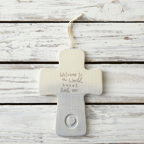 Smal white/grey cross figurine with 'welcome to the world, sweet little one' on white wooden surface