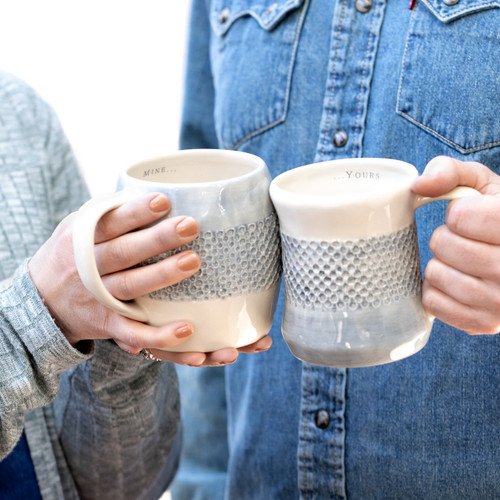 two people clinking mugs that read mine and yours on inner rim