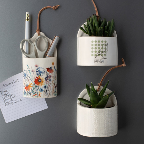 three magnetic crocks hanging on magnet board with plants and writing utensils in them and different designs on the front