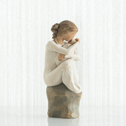 Small girl figurine wearing white dress holding baby - side view - sitting on brown rock