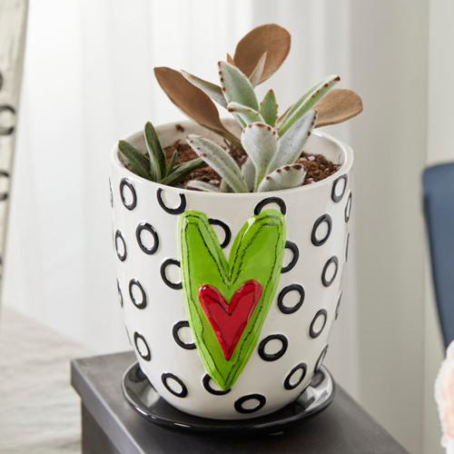 white pot with black circle pattern and green and red heart on front holding succulents