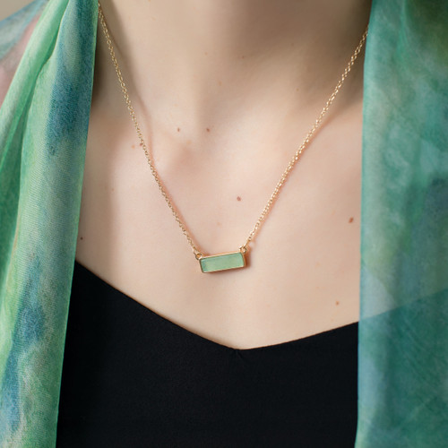 Gold necklace holds a rectangular pendant with a light green stone. Two gold, triangular earrings have light green stones. Both necklace and earrings are on a white message card with light blue accents