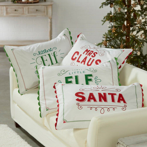 four white pillows with red and green letters reading Elf and Santa sitting on a couch