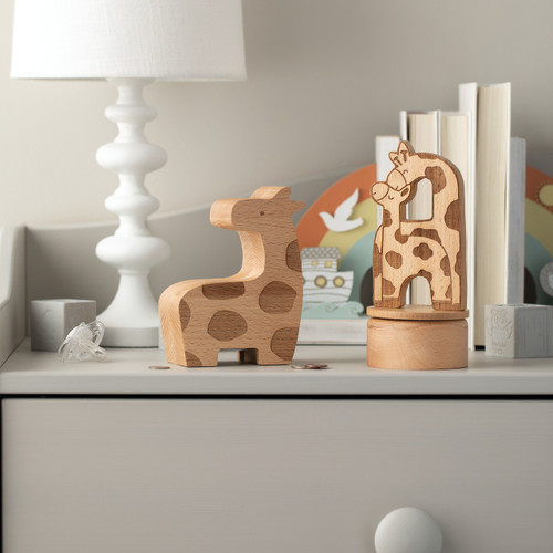 wooden giraffe bank and round wooden box with 2D wooden figure of mother and baby giraffe nuzzling each other on lid placed on gray dresser in front of white lamp, rainbow magnet board and stacks of books