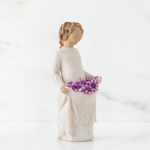 Left side view of woman with tied back, curly, light brown hair holds up a portion of her dress's skirt as it is full of purple flowers