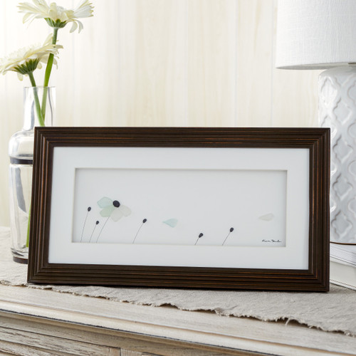 dark wooden frame sitting on dresser with pebbles depicting flowers blowing in the wind