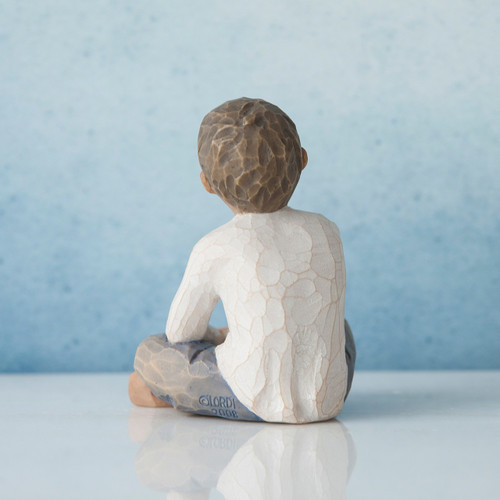 Small boy figurine sitting facing with his back to the camera in white shirt and blue jeans - blue background