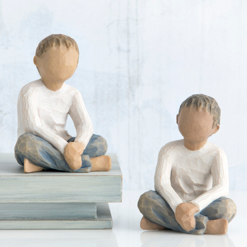 Two small boy figurines wearing white shirts and blue jeans sitting facing forward