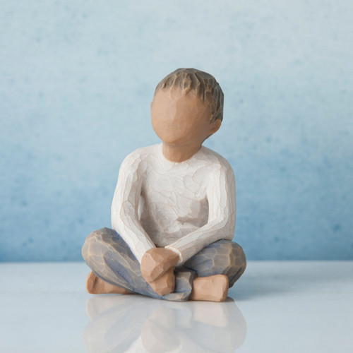 Young faceless boy figurine sitting with arms crossed on legs - blue background