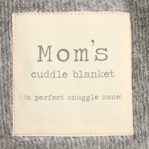 A close up image of an ivory patch that reads "Mom's cuddle blanket (a perfect snuggle zone)" on a soft gray blanket.
