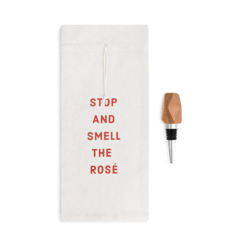 A white wine bottle bag that reads "stop and smell the rose" in red letters beside a wooden wine stopper.