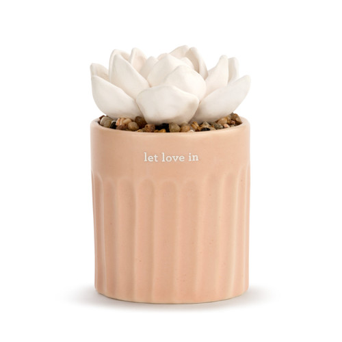 A small, stripe textured, light pink vase that reads let love in", filled with an assortment of small rocks, and a white succulent oil diffuser."