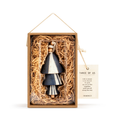 A dark blue Inspired Bell" with three pieces with cream stripes, a twine rope, and gold and wooden beads. Placed in a brown cardboard box with brown crinkle paper, and an ivory tag that reads "Three of us"."