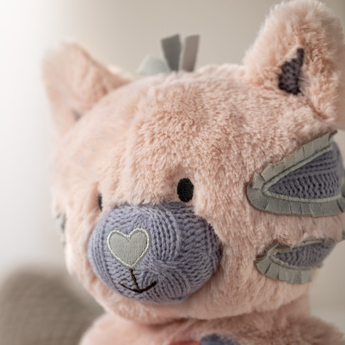 A side view close up image of a plush pink kitty with purple and gray accents.