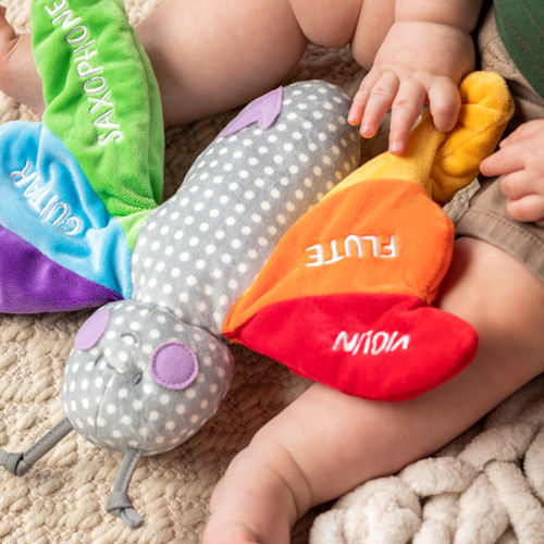 A cropped, close up image of a baby boy sitting on a floor playing with a rainbow plush butterfly.